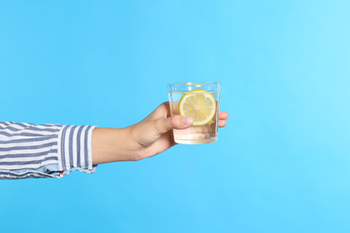 Photo of Young woman holding glass of lemon water on light blue background, closeup