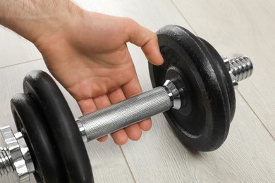 Sporty man taking dumbbell indoors, closeup. Suffering from calluses on hand