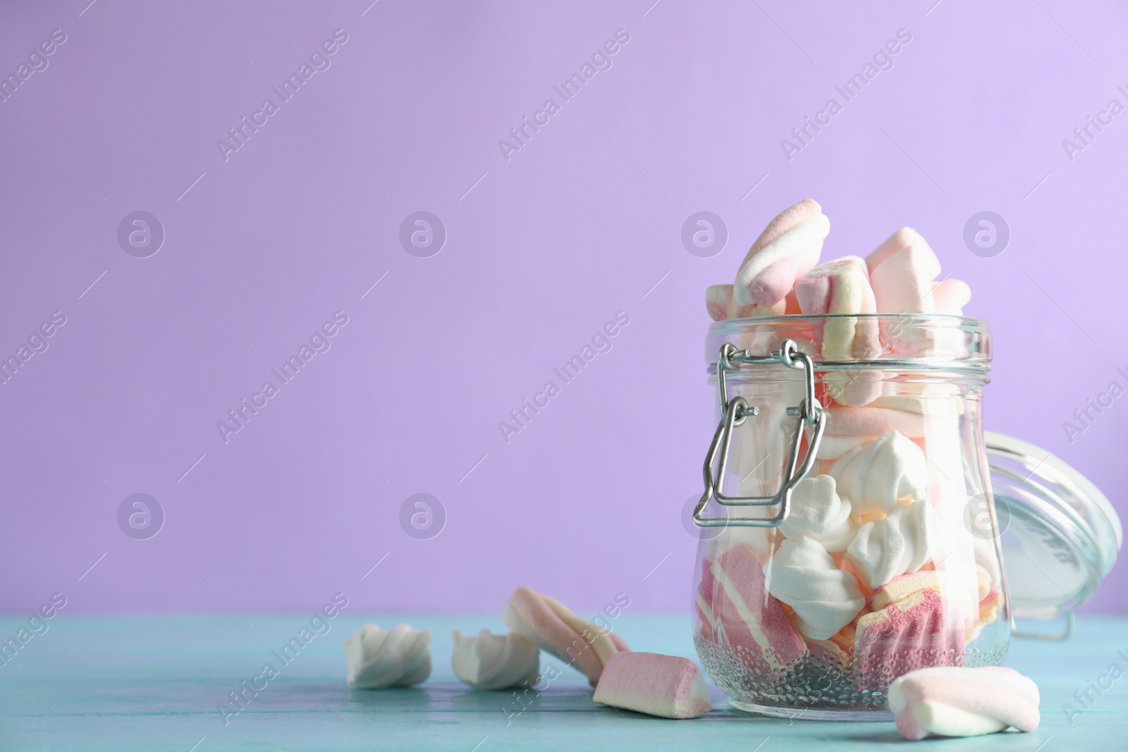 Photo of Jar with delicious colorful marshmallows on light blue wooden table, closeup. Space for text