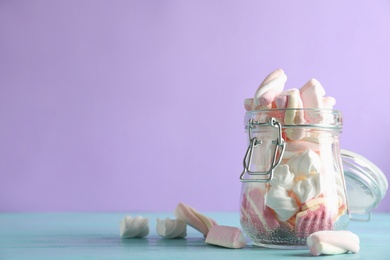 Photo of Jar with delicious colorful marshmallows on light blue wooden table, closeup. Space for text