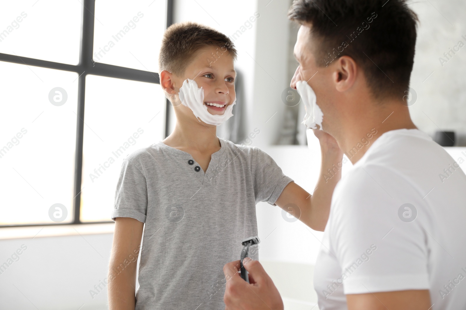 Photo of Son applying shaving foam onto father's face in bathroom