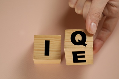 Woman turning cube with letters E and I near Q on beige background, above view