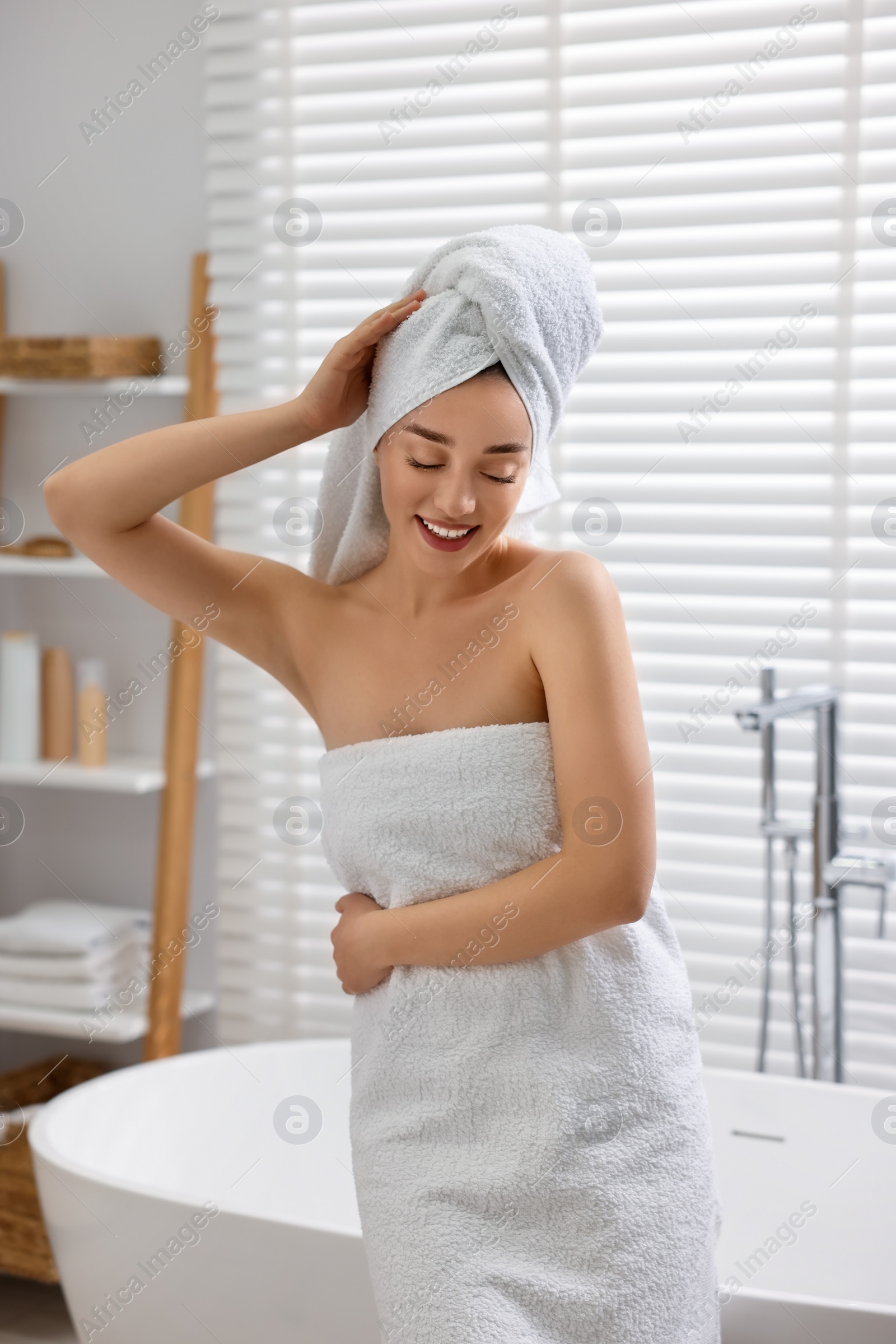 Photo of Smiling young woman near tub after shower in bathroom