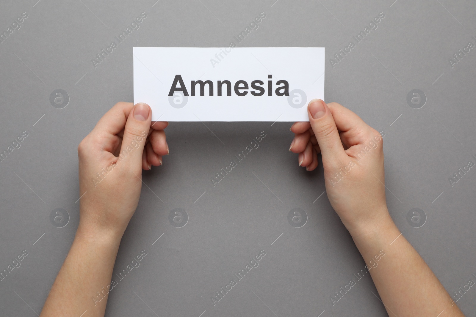 Photo of Woman holding white card with word Amnesia on grey background, top view