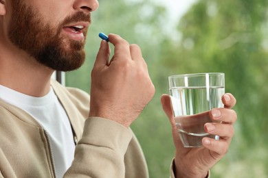 Man with glass of water taking pill on blurred background, closeup