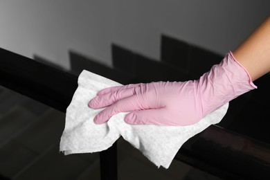 Photo of Woman in glove cleaning railing with paper towel indoors, closeup