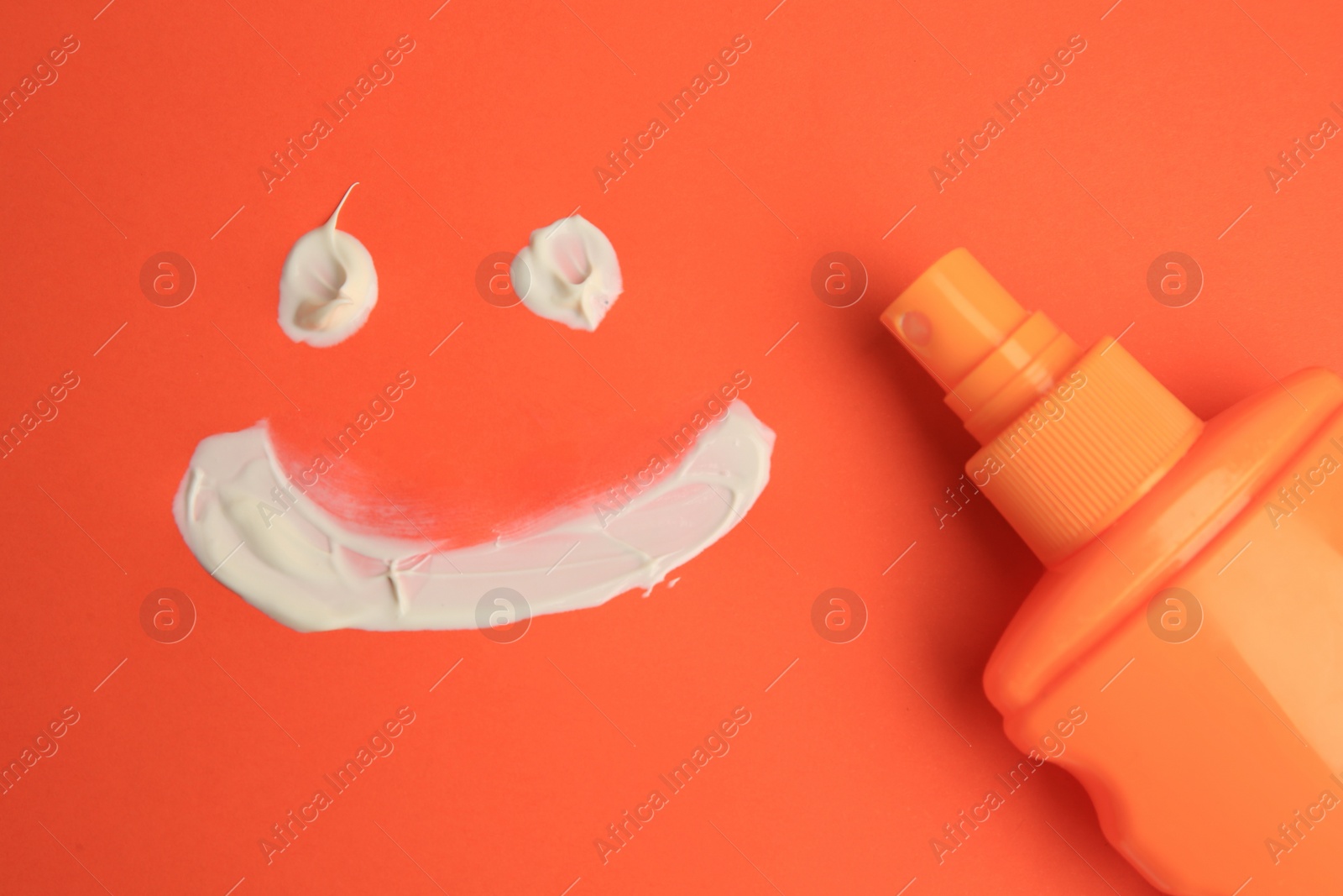 Photo of Drawing of smiling face and bottle with sunscreen on coral background, top view. Sun protection care