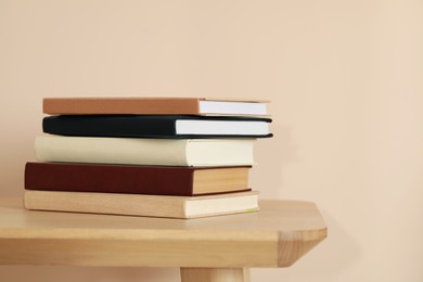 Photo of Many hardcover books on wooden table near beige wall
