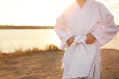 Cute little girl in kimono near river at sunset, closeup. Karate practicing