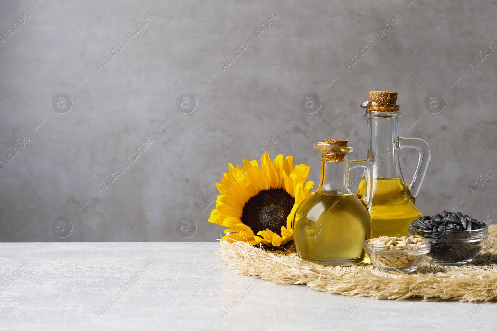 Photo of Sunflower cooking oil, seeds and yellow flowers on light grey table, space for text
