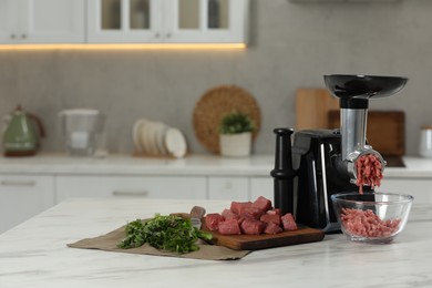 Photo of Electric meat grinder with beef mince and parsley on white table in kitchen, space for text