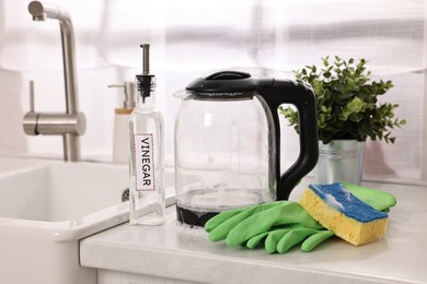 Cleaning electric kettle. Bottle of vinegar, rubber gloves and sponge with foam on countertop in kitchen