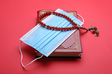 Photo of Muslim prayer beads, Quran and medical mask on red background