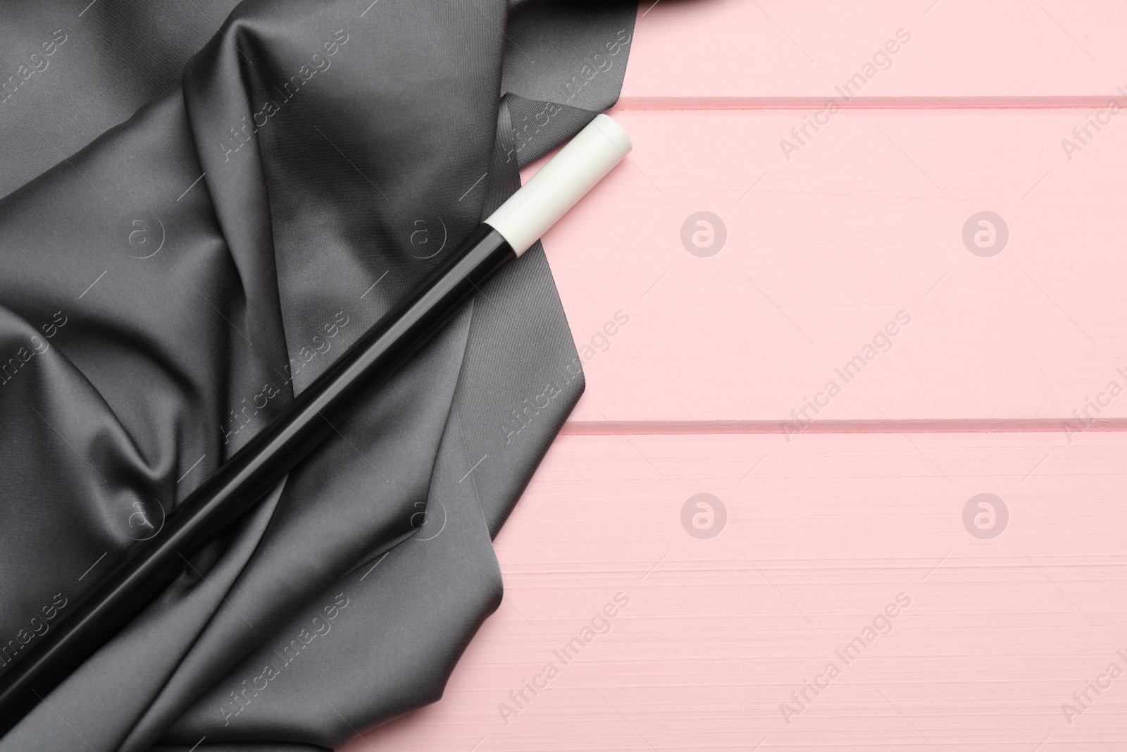 Photo of Beautiful black magic wand and grey fabric on pink wooden table, top view. Space for text
