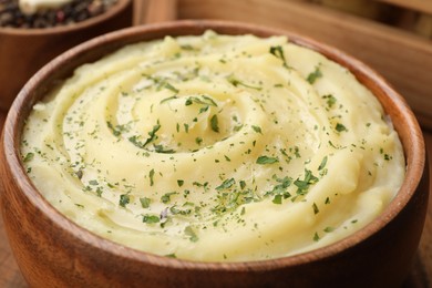 Photo of Bowl of tasty mashed potato with greens on wooden table, closeup