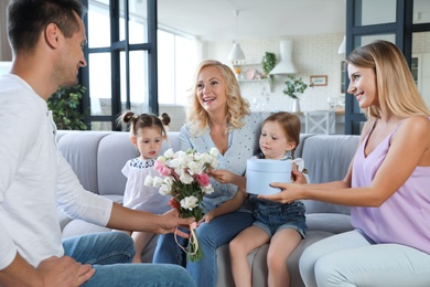 Photo of Happy family with little children congratulating mature woman in living room
