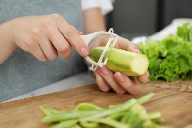 Photo of Woman peeling fresh zucchini at table, closeup