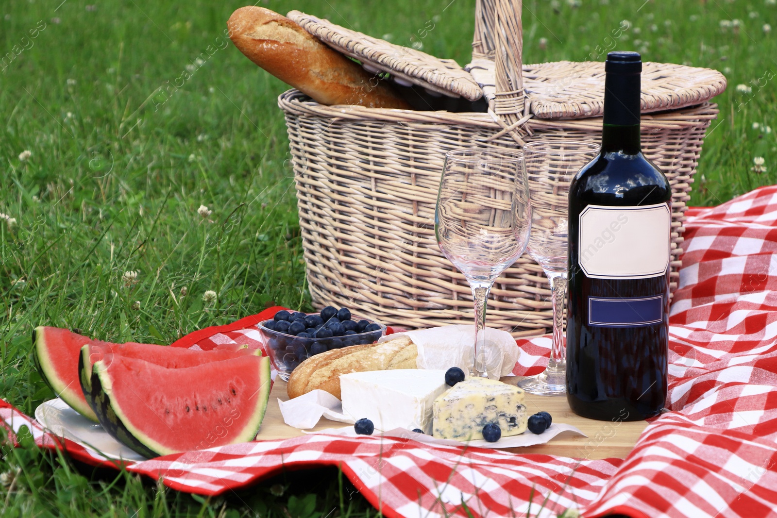 Photo of Picnic blanket with delicious food and wine outdoors on summer day