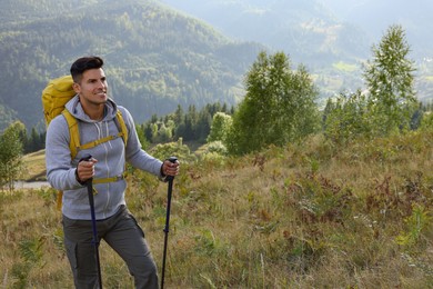 Photo of Tourist with backpack and trekking poles hiking through mountains, space for text