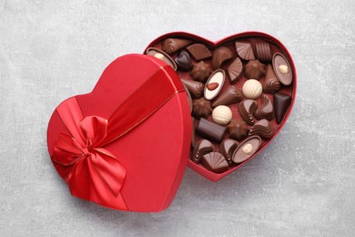 Photo of Heart shaped box with delicious chocolate candies on light grey table, top view