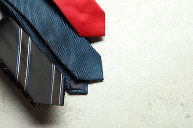 Photo of Different neckties on light textured table, flat lay. Space for text