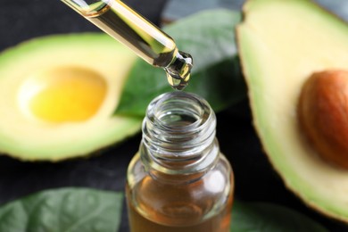 Dripping essential oil into bottle near cut avocado, closeup