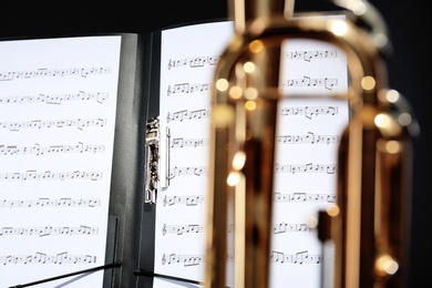 Photo of Music note sheets on black background, closeup view through blurred trumpet