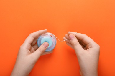 Photo of Woman holding container with dental floss on orange background, top view