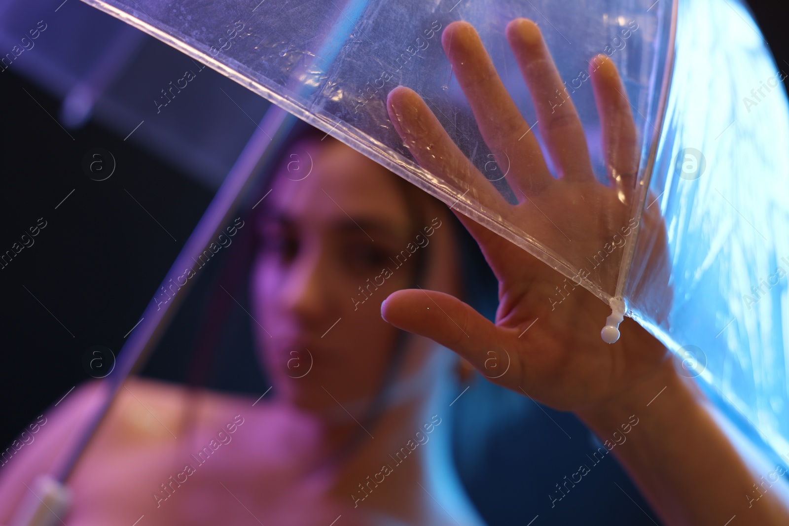 Photo of Beautiful woman with umbrella on dark background in neon lights, selective focus