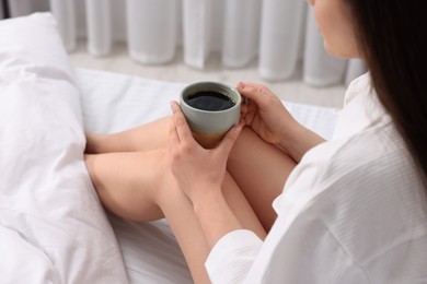 Photo of Woman with cup of drink on bed at home, closeup. Lazy morning