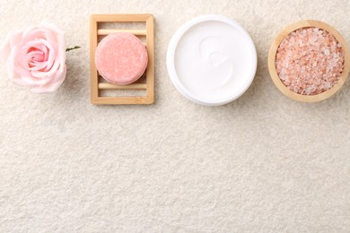 Flat lay composition with moisturizing cream in open jar and other body care products on light textured table. Space for text