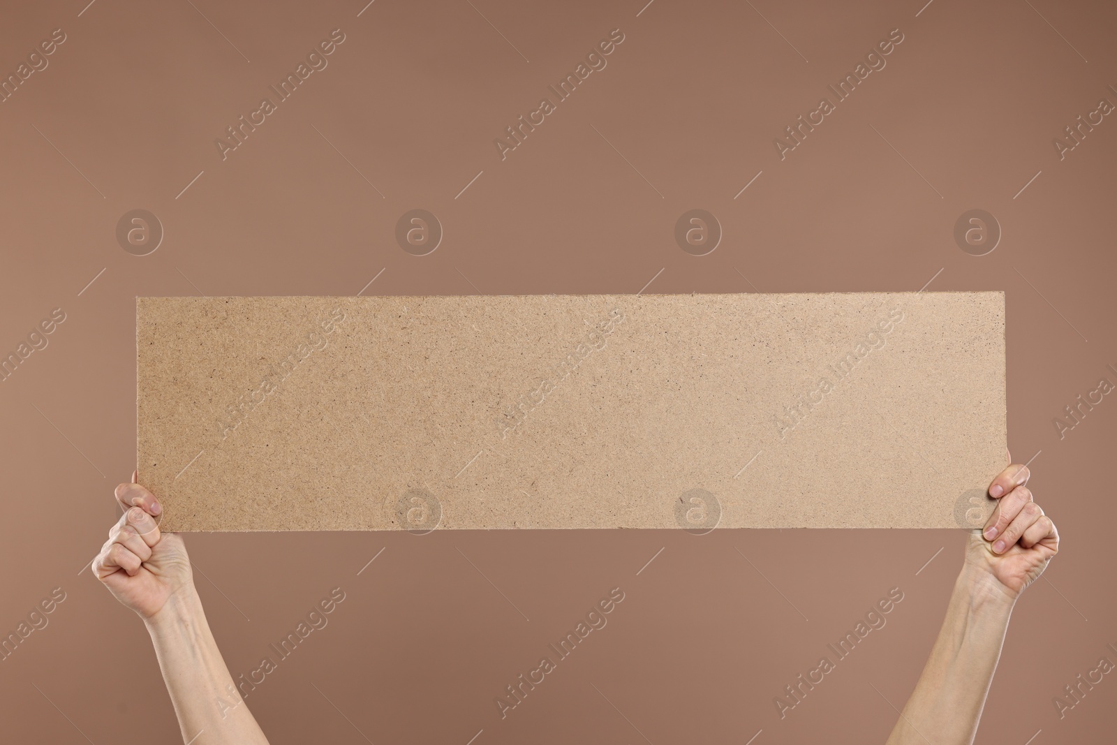 Photo of Woman holding blank cardboard banner on brown background, closeup. Space for text