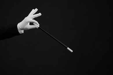 Magician holding wand on black background, closeup. space for text