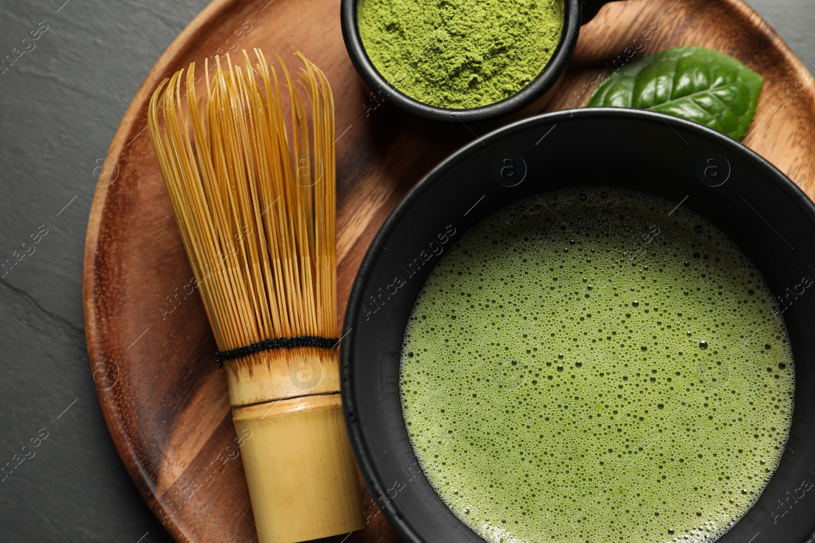 Photo of Cup of fresh matcha tea, bamboo whisk and green powder on black table, top view