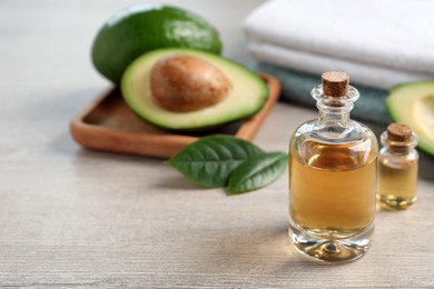 Photo of Bottles of essential oil, fresh avocado and towels on light wooden table, space for text