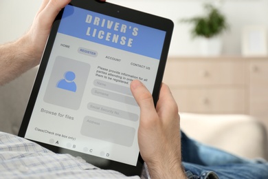 Photo of Man using tablet to fill driver's license application form at home, closeup