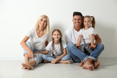 Photo of Happy family sitting on floor near white wall