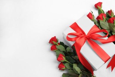 Photo of Beautiful gift box with bow and red roses on white background, above view. Space for text