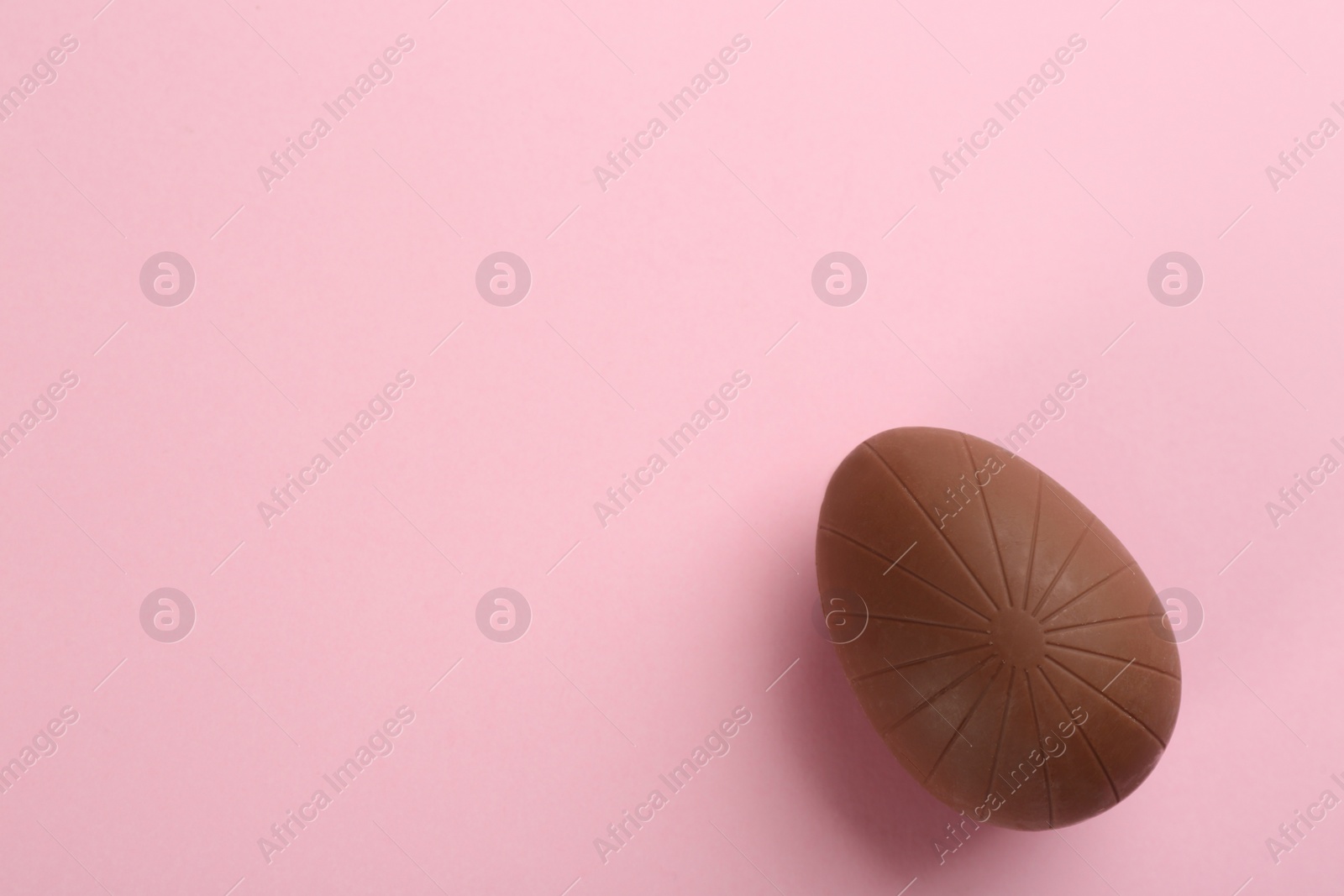 Photo of Sweet chocolate egg on pink background, top view. Space for text