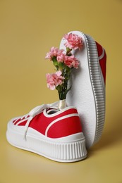 Photo of Pair of red classic old school sneakers and carnation flowers on yellow background