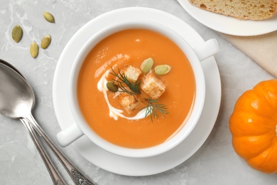 Photo of Tasty creamy pumpkin soup with croutons, seeds and dill in bowl on light grey table, flat lay