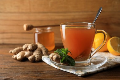 Cup of delicious ginger tea and ingredients on wooden table, space for text