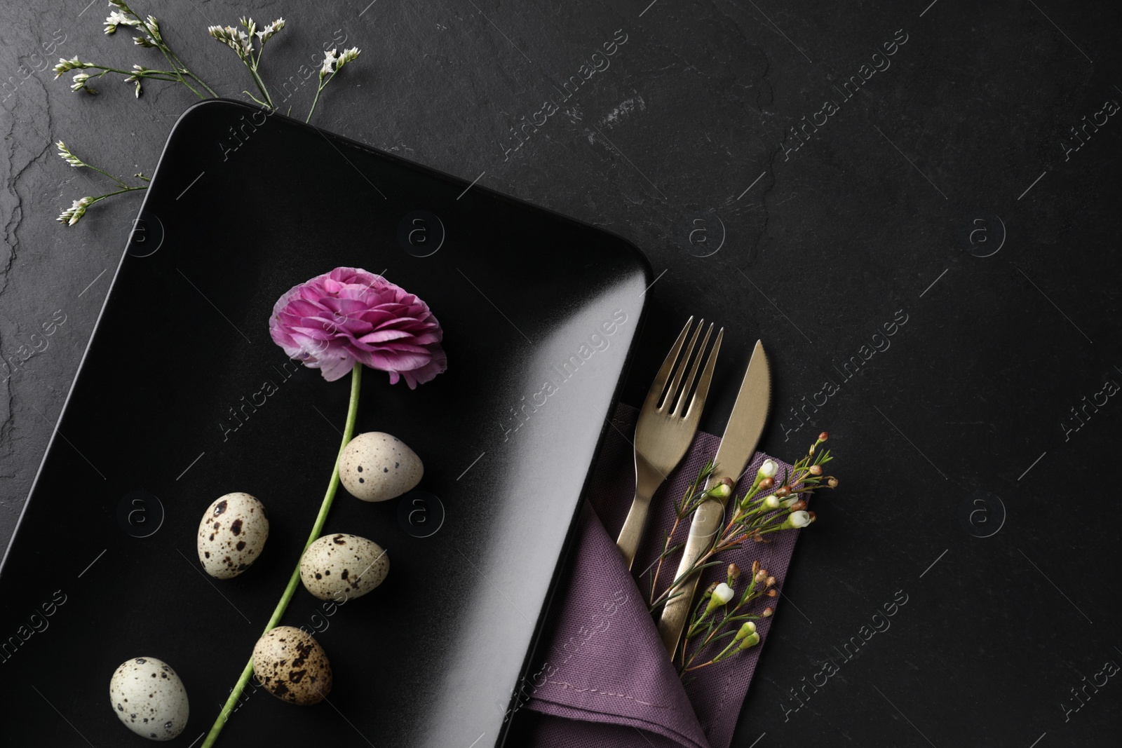 Photo of Festive Easter table setting with quail eggs and floral decoration on dark background, flat lay