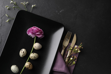 Festive Easter table setting with quail eggs and floral decoration on dark background, flat lay