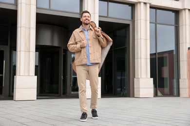 Photo of Attractive happy man holding garment cover with clothes outdoors. Dry cleaning service