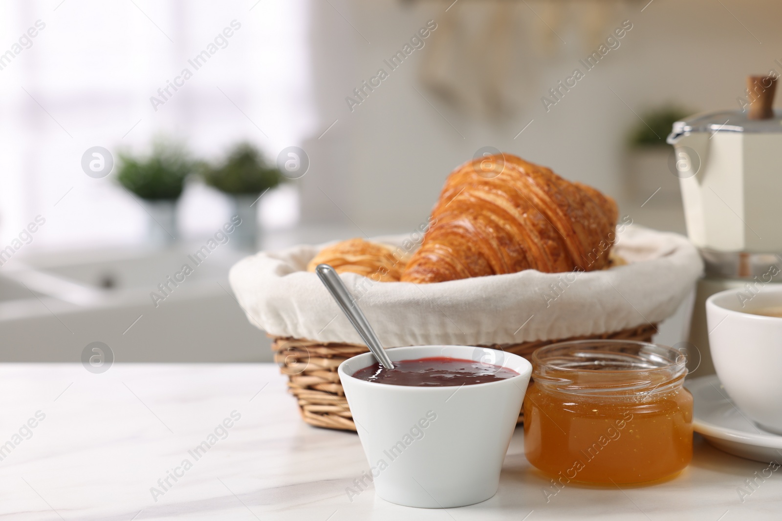 Photo of Breakfast served in kitchen. Fresh croissants, jam, honey and coffee on white table, space for text