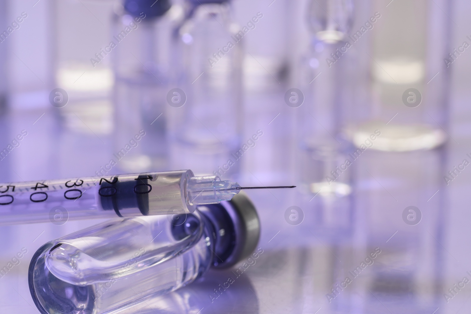 Photo of Glass vial and syringe with medication on white table, closeup. Space for text