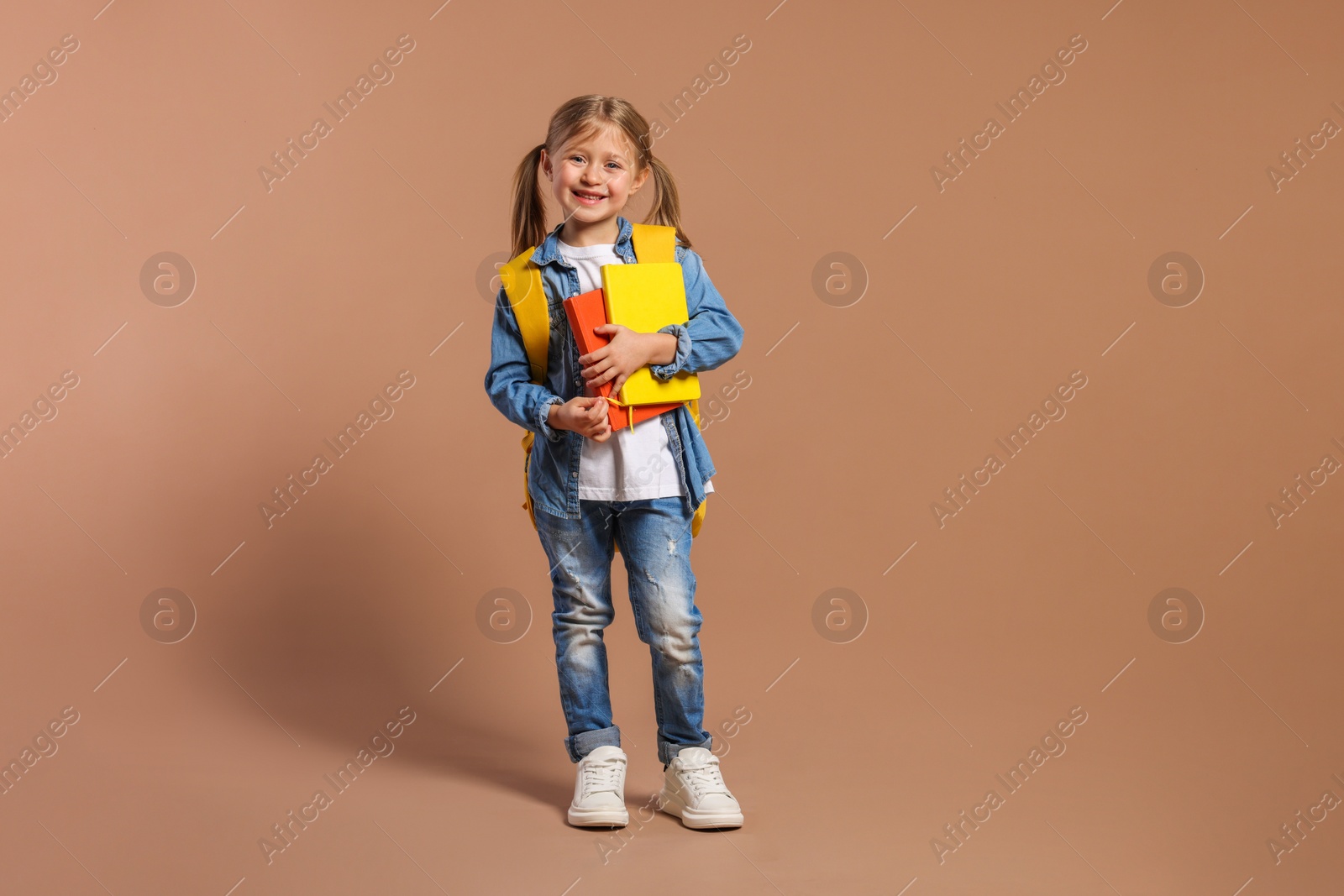 Photo of Happy schoolgirl with backpack and books on brown background