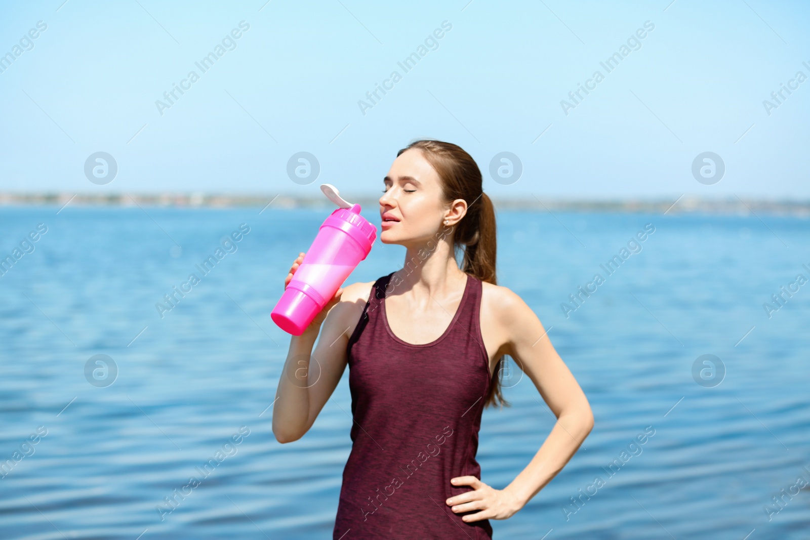 Photo of Athletic young woman drinking protein shake at riverside