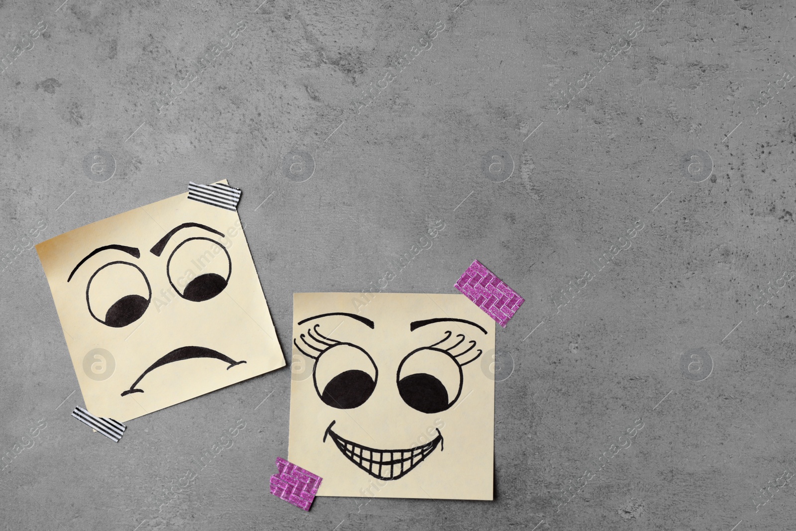 Photo of Paper notes with drawn faces on grey background, flat lay with space for text. Concept of jealousy